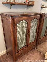 Front view of wooden cabinet showing two doors with wire insert and fabric curtains, drawer at bottom.