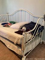 Full view of the white metal frame daybed with pillow, blanket, and mattress under sheet.