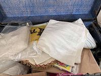 Pile of assorted linens including table cloths, towels, sheets, some are folded and some still in plastic packaging