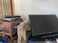 Photo showing Dell monitor with black frame and cables, Samsung Blu-ray and VHS/DVD players stacked on rattan shelf.