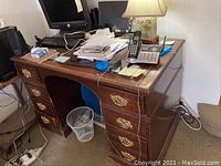 Wood desk showing gold tone drawer pulls, heavy wear such as nicks and marks, cluttered with electronics and papers