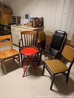 Group photo of wood and vinyl chairs along with a small red folding stool in basement setting