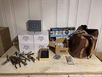 Full view of group showing six TCP LED lightbulb boxes, assorted hand tools with rust, various boxed items including solar charger, and brown canvas tool bag.