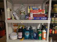 Full shelf with various cleaning liquids, mouthwash, ketchup bottle, paper plates, boxed food storage products, and foil.