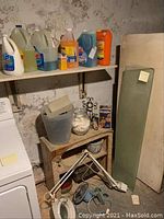 Photo of cleaning product containers on white shelf above wood shelf with several household items