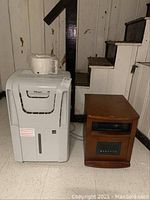 Photo shows the Danby Premiere dehumidifier and electric heater side by side on tile floor near basement stairs.