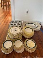 Overview of stacked plates, bowls, cups, saucers and two platters on hardwood floor