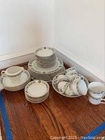 Overall view of the china collection including stacked plates, tea cups with saucers, a creamer, and bowls arranged on a hardwood floor.