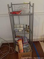 Full view of the metal shelving unit showing all shelves and items including boxed goods on the floor and candles on shelves