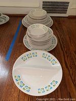 Stack of assorted size vintage Ironstone plates with blue, green, and yellow decorative border pattern, showing wear and stains.