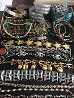 Photo showing multiple bracelets in various styles, materials including metal, brass, chain links, and crystals, arranged flat in a box.