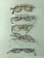 Five pairs of vintage eyeglasses arranged vertically on green surface.