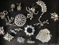 Photo of 12 vintage rhinestone jewelry pieces arranged on black background, showing variety of pins and earrings.