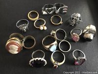 Top-down view of all 16 costume and statement rings arranged on black background for full lot display.