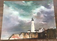 Full view of the oil painting featuring a lighthouse on a rocky coastline with cloudy sky backdrop.