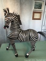 Full side view of the hand carved wooden zebra showing painted black and white stripes, horsehair mane and tail, and stance.