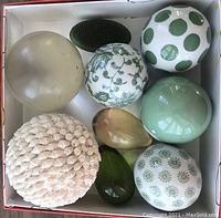 Top-down view of all 9 items arranged in a white box, showing variety of balls, eggs, shell ball, and flower frog.