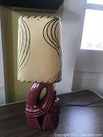 Front view of the lamp with the shade attached, showing the burgundy ceramic base with floral design and the cream shade with black stripes.