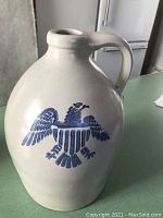 Front view of white ceramic jug with blue American eagle insignia and handle.