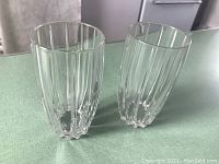 Pair of tall clear crystal highball glasses with vertical omega cuts, standing side by side on a surface.