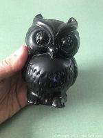 Front view of the small black cast iron owl held in hand, showing detailed design on eyes, beak, and body feathers.