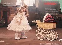 Box showing the doll dressed in period clothing next to the baby carriage inside a historic setting background.