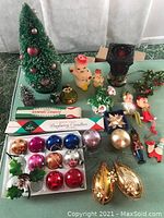 Wide view of assorted vintage Christmas items including bottle brush trees, Santa candles, elves, candleholder, Bayberry candle boxes, bulbs, and ornaments on a green cloth.