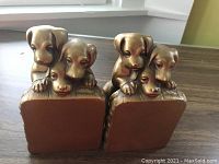 Front view of both vintage pot metal puppy dog bookends showing three puppies on each with some damage to one puppy's head per bookend.
