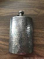 Full view of the front side of the hammered silver plated flask showing the engraved panel and screw-top cap.