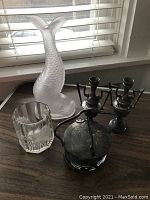 Overview of full lot showing the frosted glass fish decanter, silverplated lidded mustard jar, etched glass spooner, and two silverplated candleholders or bud vases.