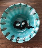Top view of an aqua colored art glass bowl showing the pattern of black and white dots and unique black shapes inside.