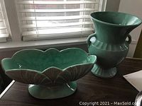 Green pottery urn vase and flowerbox on a dark wood table near window with blinds, showcasing their shapes and glaze color.