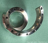 Close-up photo of polished silver-tone spiral candleholder with circular holes along the spiral and smooth reflective finish, showing modernist design.