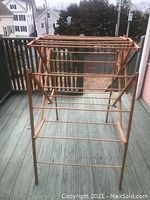 Full view of a wooden sweater drying rack standing on a green painted wooden porch floor, showing it open with multiple horizontal rods for drying.