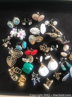 Photo showing an assortment of vintage screwback earrings laid out on a black surface. Includes floral, heart, pearl, cameo, and stone designs.