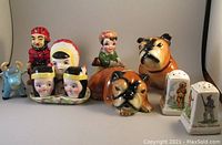 Front view of all 10 Americana-themed ceramic salt and pepper shakers on flat surface including Paul Bunyan, Babe the Blue Ox, a dog Bulldog, Native American babies molds, and two white Royal Winton Old Canada shakers.