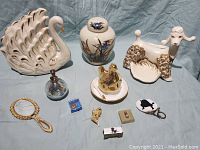 Overview of 11 vintage vanity and decorative items showing swan lamp, poodle holder, ginger jar, hen dish, perfume atomizer, mirror, purses, jewelry, and other small vanity items on blue cloth.