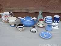 Photo showing 12 pieces of English pottery including Wedgwood Jasperware teapot, plate, candle holder and vase, and assorted Devon Pottery pieces including floral teapot, pitcher, small mugs, and cottage figurine