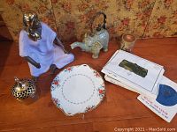 Full view showing all items on wooden surface with floral fabric background, includes statue, teapot, plate, silks, brass container, and onyx box