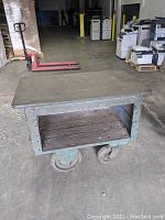 Front view showing the wooden platform with steel framing and open storage space below, large metal caster wheels visible