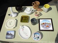Full view of 16 assorted vintage ceramics and pottery items arranged on a table including teapot, mugs, decorative plates and vases.