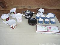 Full overview of all items arranged on a surface including teapot in center, multiple cups, saucers, and trinket dish.