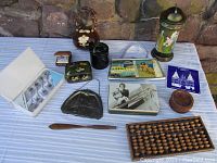 Photo showing the full lot on a striped tablecloth with stone background. Items include abacus, various souvenir purses, box, coasters, decanter, plaque, and travel clock.
