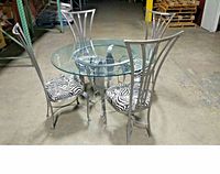 Dining set with round glass table and 4 zebra print padded high-back brushed steel chairs, shown from side angle