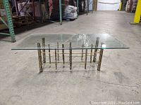 Front angled view showing glass top on torch cut metal base with concrete warehouse floor background.