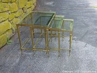 Side view of three nested brass and glass tables showing sizes and clear glass tops with brass frames.