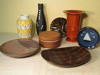 Front view of all seven pottery items arranged on a neutral surface: four vases/containers and three plates with varied colors and designs.