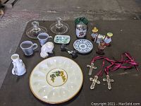 Photo of the entire lot showing multiple vintage collectibles including deviled egg plate, glass candle holders, ceramic figurines, silverplated crosses and rattle.