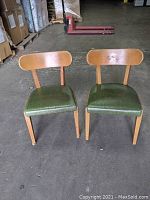Front view of two mid-century dining chairs, wooden frame with green upholstered seats, one with casters.