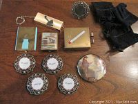 Top view of five small photo frames, four vintage compacts, umbrella bag carrier, black pouch, and small decorative mirror on wooden surface.